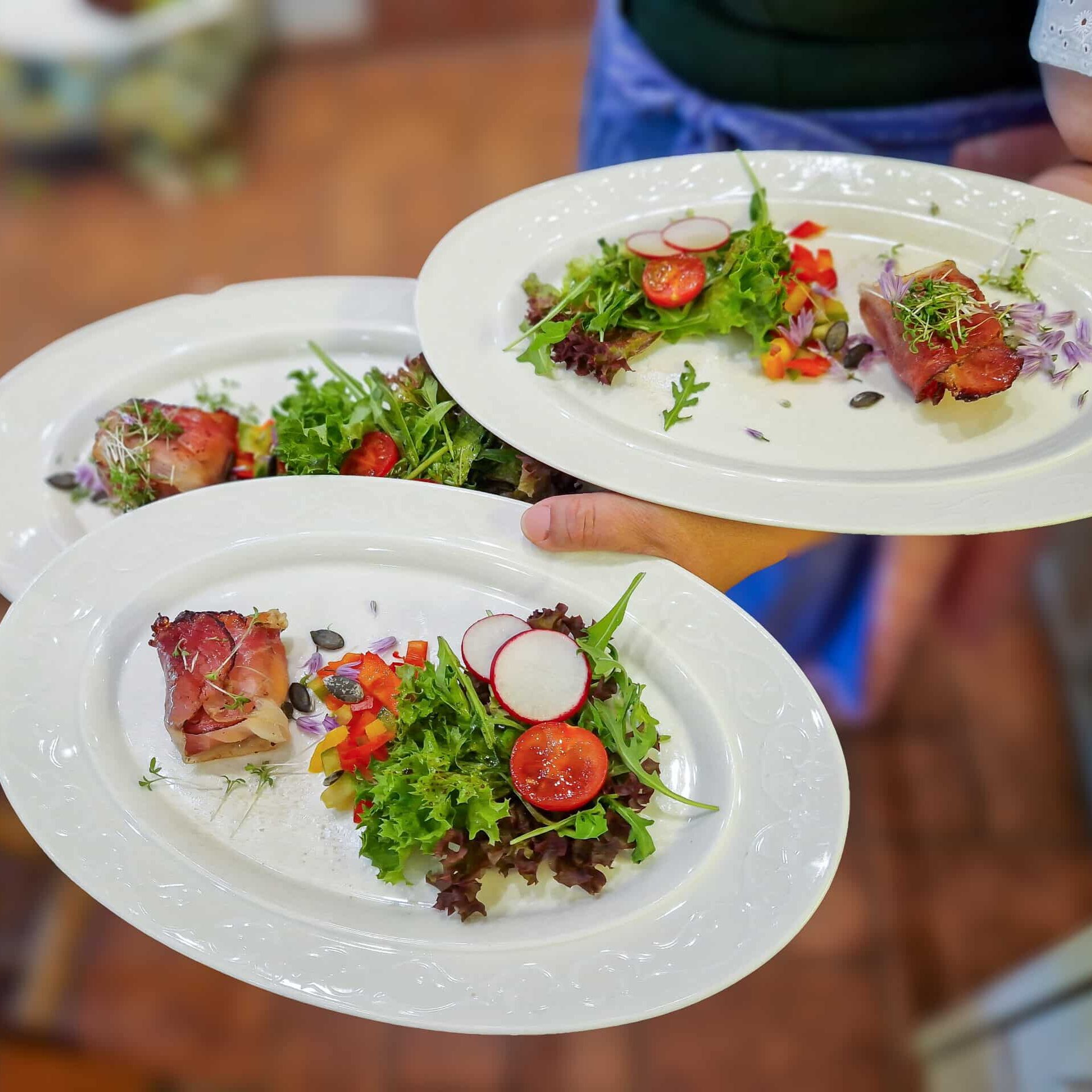 Frau in Tracht serviert drei Teller mit Salatvorspeise