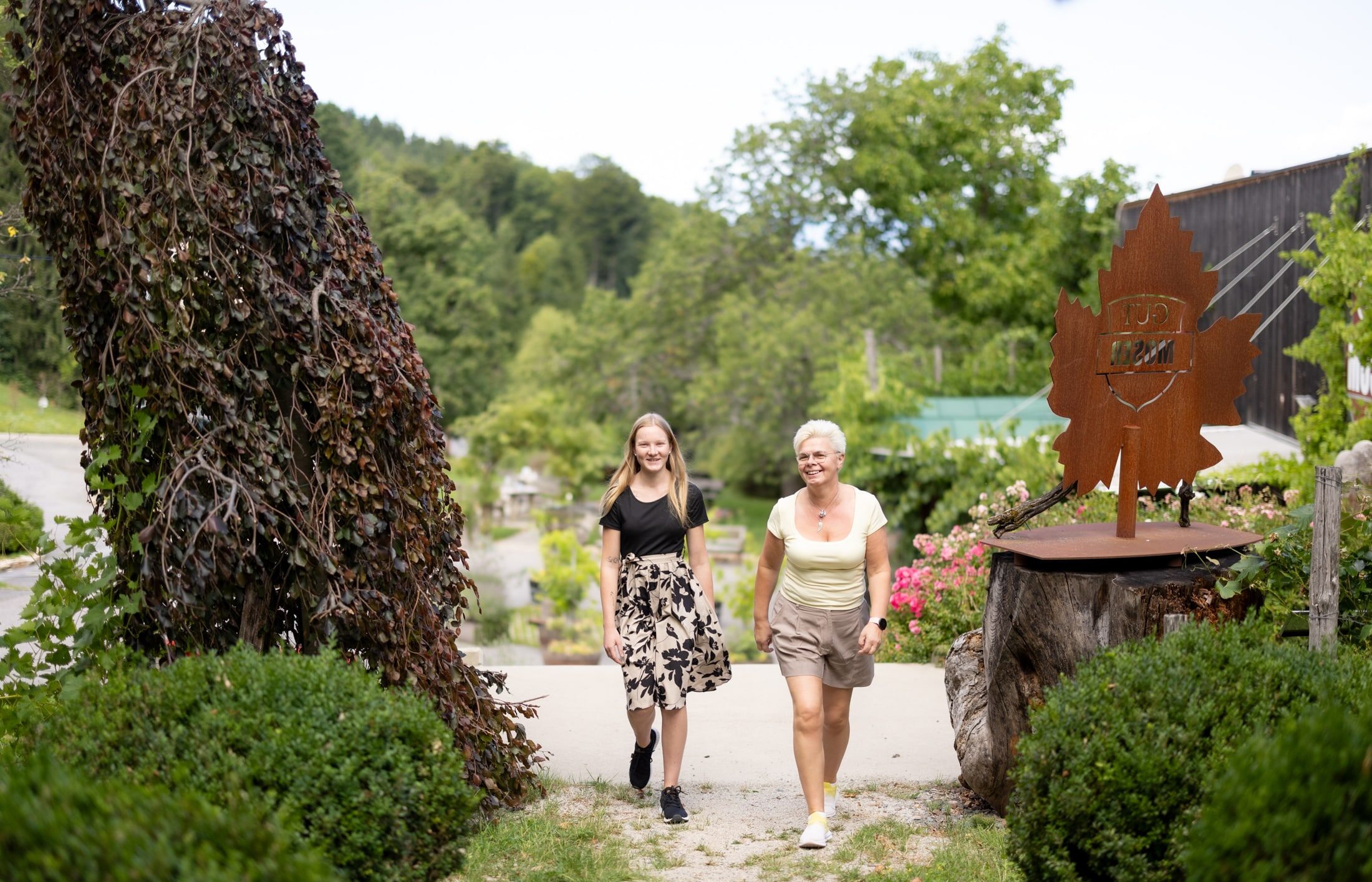 Ältere Frau geht mit Mädchen durch Garten des Gut Moser spazieren