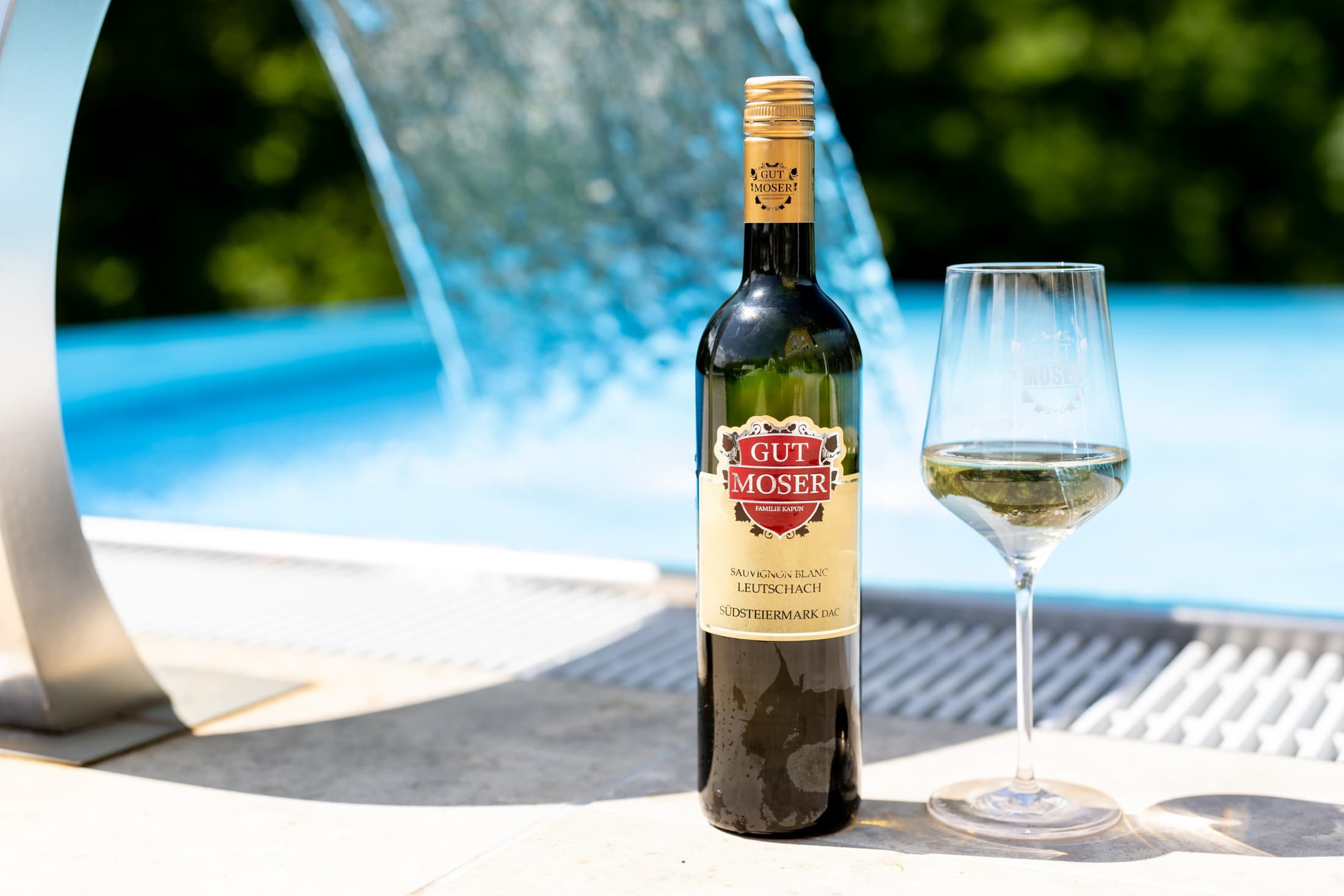 Flasche Wein mit Weinglas steht am Beckenrand des Pools